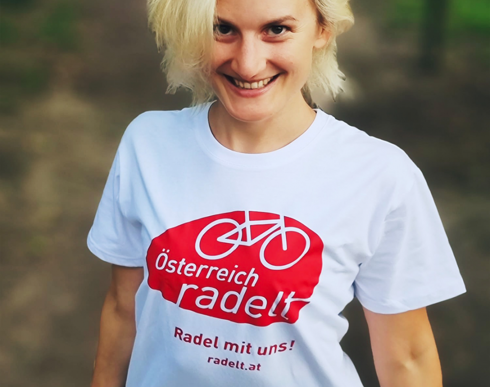 Österreich radelt Tshirt Lächelnde Frau mit weißem T-Shirt auf dem das Österreich radelt Logo gedruckt ist.
