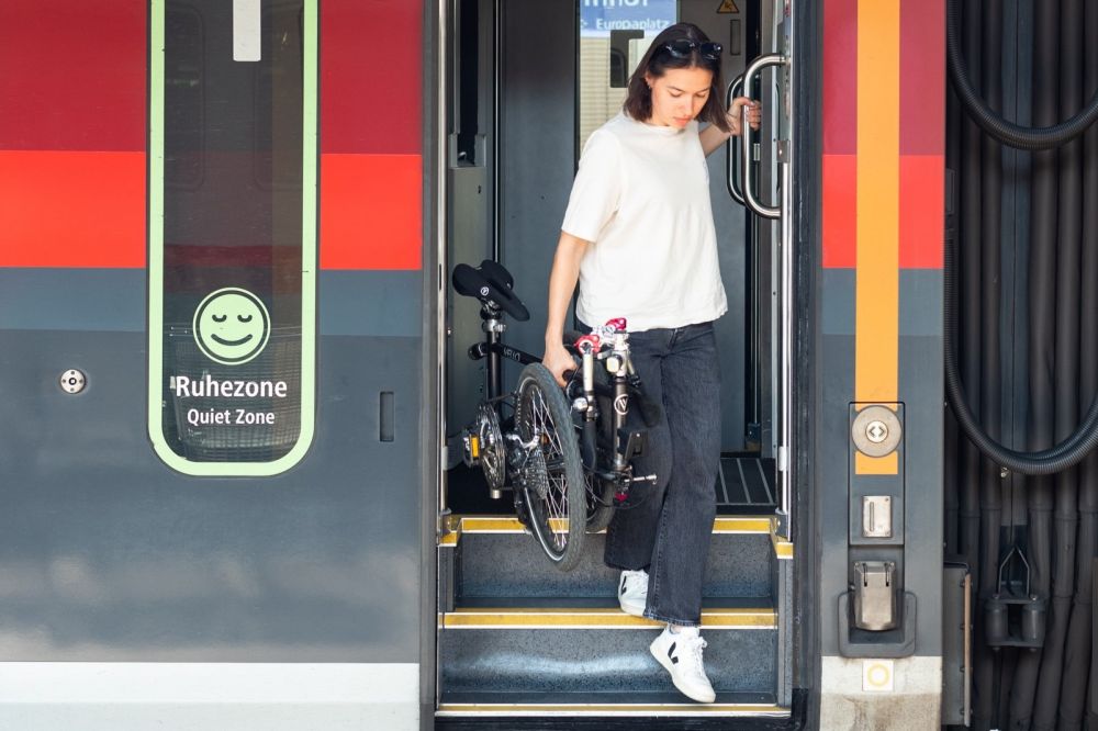 Frau steigt mit zusammengeklapptem VELLO Faltrad aus einem Zug aus
